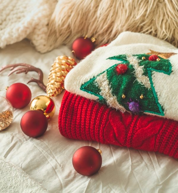 Two winter sweaters laid on a bed with pillows and New Year's decorations.